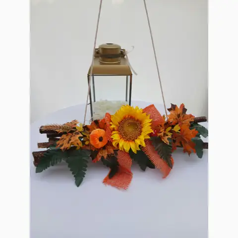 Hängedeko mit Sonnenblume und Herbstlaub vor einer goldfarbenen Laterne